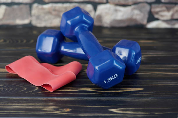 istock two blue hand weights beside a red elastic exercise band against wooden background 1216448886