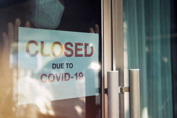 business office or store shop is closed/bankrupt business due to the effect of novel coronavirus (covid-19) pandemic. unidentified person wearing mask hanging closed sign in background on front door. - business closed imagens e fotografias de stock