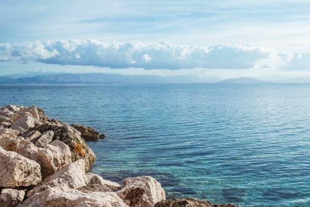 Amazing bay with crystal clear water and big stones on Corfu island, Greece. Beautiful landscape of Ionian sea beach. Sunny weather, blue sky.