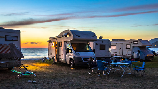 Campers and Motorhomes overlooking sunset in the Mediterranean sea from their campsite on the beach, Corsica, France