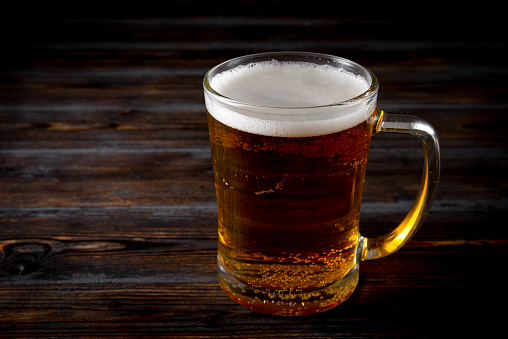 1 mug of light beer on a wooden background, side view,