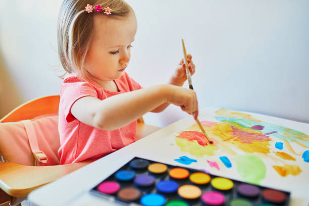 istock Girl drawing rainbow with colorful aquarelle paints 1216455231