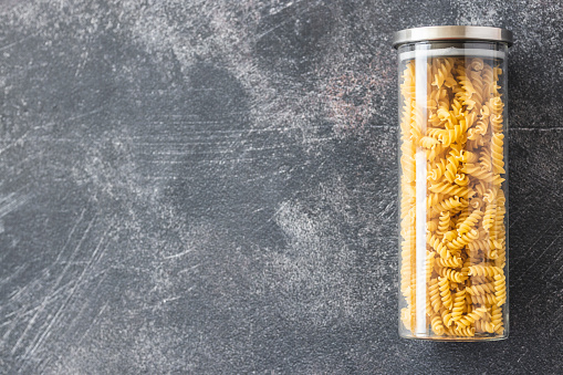 Uncooked pasta in airtight jars on dark background