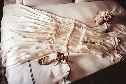 A wedding dress with shoes, a bouquet and accessories laid on a bed.
