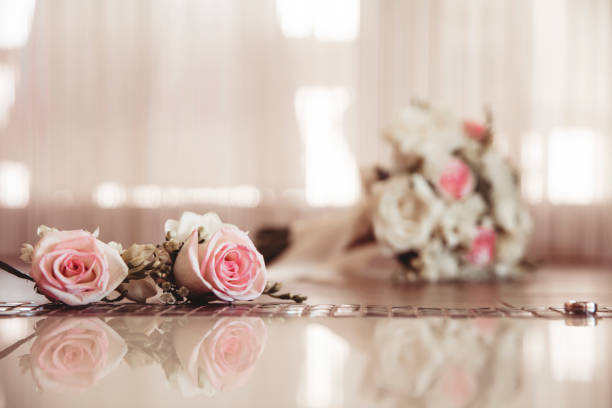 Two bright roses and a ring on a reflective surface.