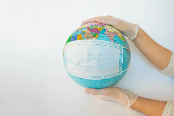 Earth globe dressed in the protective mask on the hands of a man in protective gloves. Symbol that people all over planet are quarantined due to epidemic and pandemic of Coronavirus. White background.