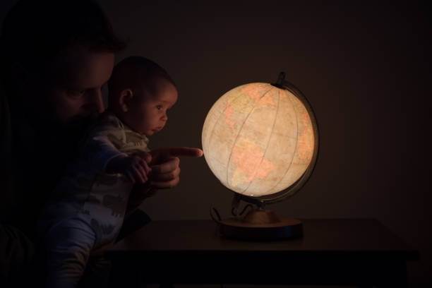 Father holding his baby and pointing with his finger on the globe