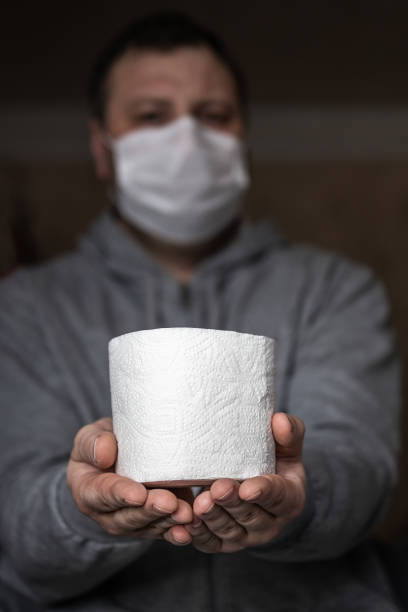 un hombre enmascarado está sosteniendo un rollo de papel higiénico en sus manos. enfoque selectivo. pánico y escasez en las tiendas del coronavirus depmidense mundial - people purity personal accessory handkerchief fotografías e imágenes de stock