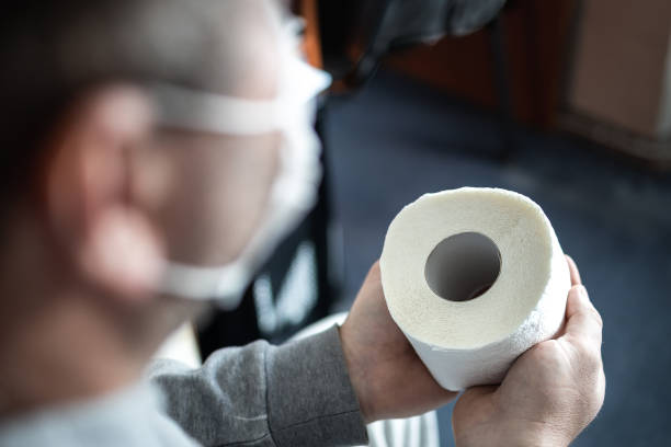 un homme masqué tient un rouleau de papier hygiénique dans ses mains. mise au point sélective. panique et pénurie dans les magasins du coronavirus pandémique mondial - la folie douce photos et images de collection