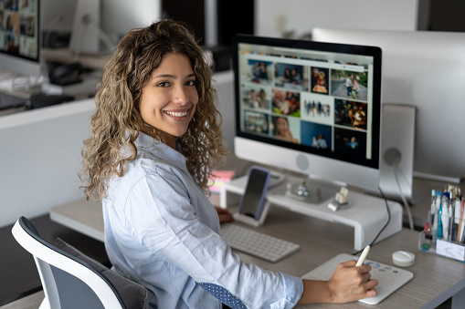 Happy woman editing images at a creative office and looking at the camera smiling. **PHOTOS ON SCREEN BELONG TO US**