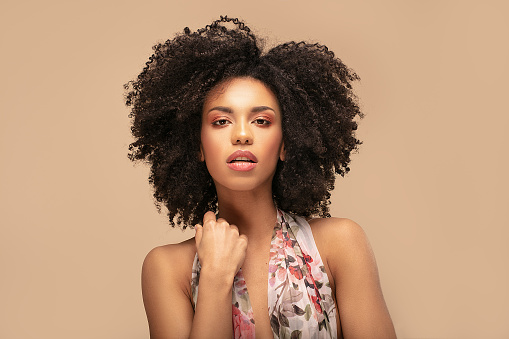 Beauty portrait of beautiful emotional african american girl with curly hair on beige studio background.