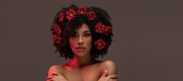 Young attractive afro woman with beautiful flowers in hair and lips. Beauty studio portrait.