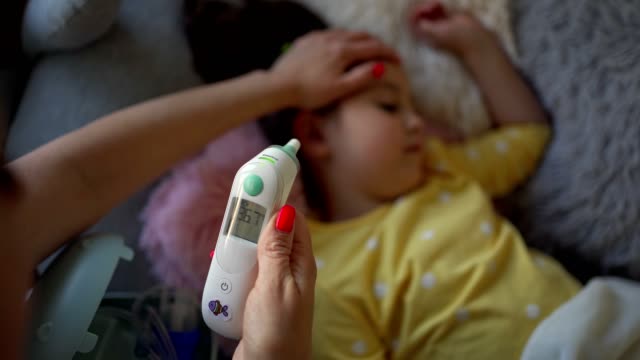 Caring mother measuring her daughter temperature with digital thermometer and she is healthy now