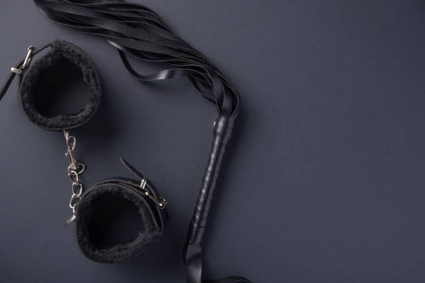 istock Accessories for bdsm on a black background. Leather lash and leather handcuffs. Valentine's Day. Erotic shop. Copy space 1216486164