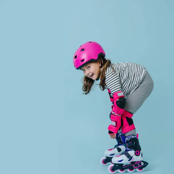 Photo of Happy little girl in roller skates with pink protective gear over blue