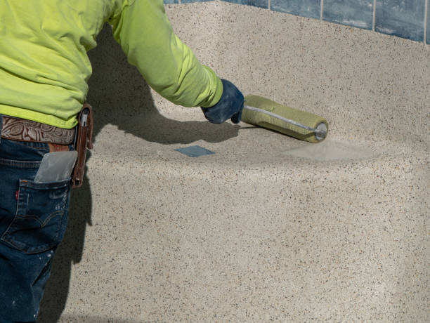 Man using a roller to remove excess water from newly applied swimming pool cement containing pebbles