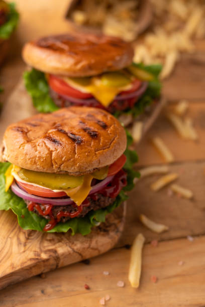 istock Hot cheeseburger on a wooden cutting board. Burger with beef, cheese, vegetables, crispy buns and salt fries on a rustic table. Fast food concept. 1216504332
