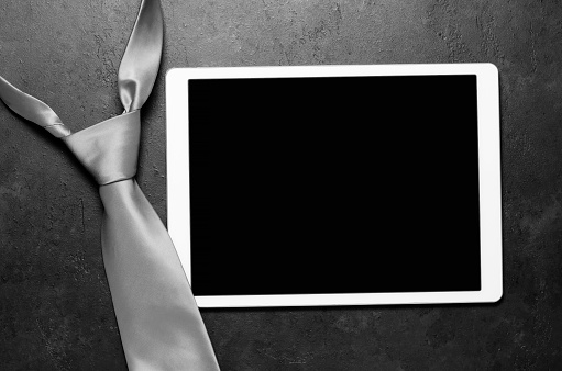 Men's tie and tablet. Black concrete background. Copy space.