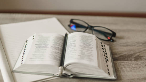 Top view of table with bile, blank notebook, pencil and eyeglasses.