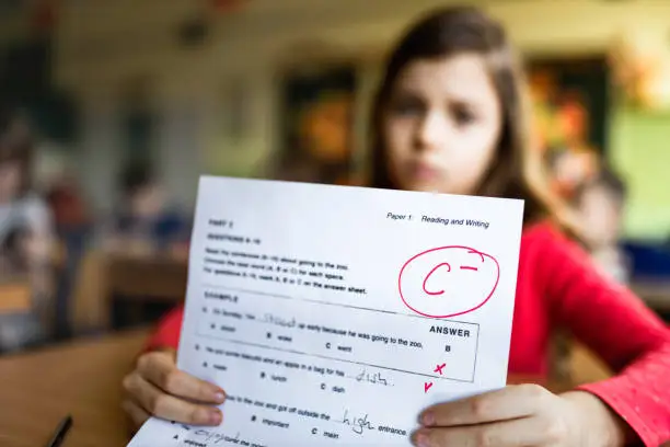 Close up of a schoolgirl showing her C- grade on a test at elementary school.