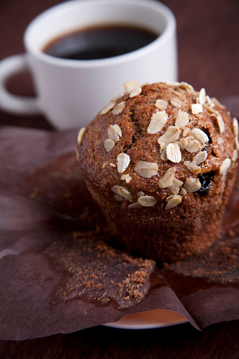 One delicious gourmet oats and raisin bran muffin served alongside a hot cup of black coffee.