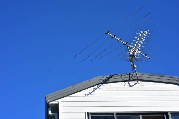 Multi channel aerial above roof of wooden house with clear blue sky in background.