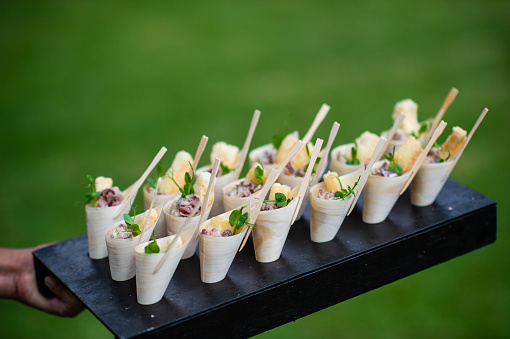 Fried Calamari Scampi Appetisers canapes being presented in bamboo cones and served at a party with selective focus.  It is being served at a wedding party.  A waiter is holding the tray with canapes.