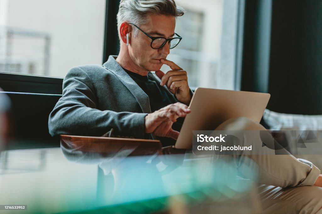 Businessman reading emails in office lobby Businessman looking at laptop and thinking. Businessman reading emails on laptop in office lobby. Business Stock Photo
