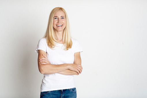 Laughing blonde middle-aged woman posing with arms folded isolated on white background, free space