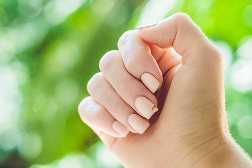Broken nail on a woman's hand with a manicure on a green background