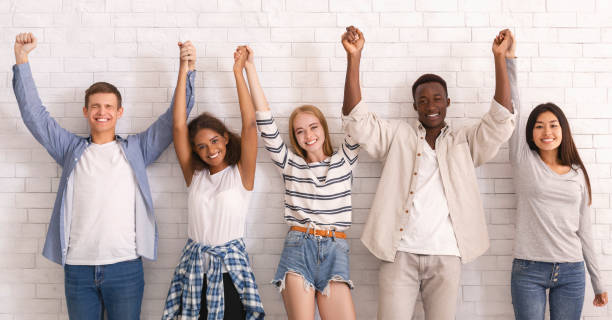 istock Happy friends standing over white brick wall, uniting hands together 1216542905