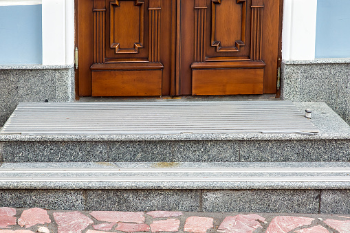 gray granite threshold with steps covered with non-slip rubber strips at the entrance wooden door of brown color at the facade of the building, front view close up.