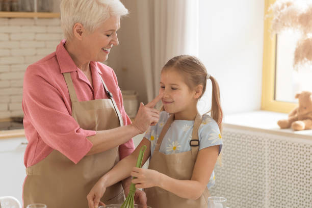 istock Fun baking time. Happy older lady touching her granddaughter's nose in kitchen, empty space 1216546569