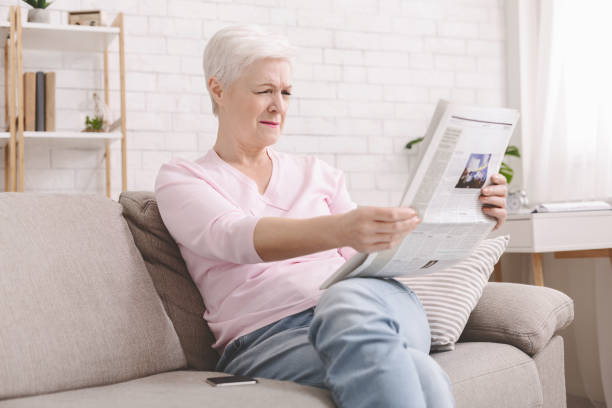 istock Senior lady squinting and holding newspaper far from eyes 1216546852
