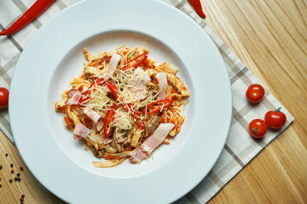 istock Appetizing, homemade pasta (tagliatelle) with white sauce, cheese, vegetables, bacon in a white plate on a wooden background. Traditional italian food. 1216552567