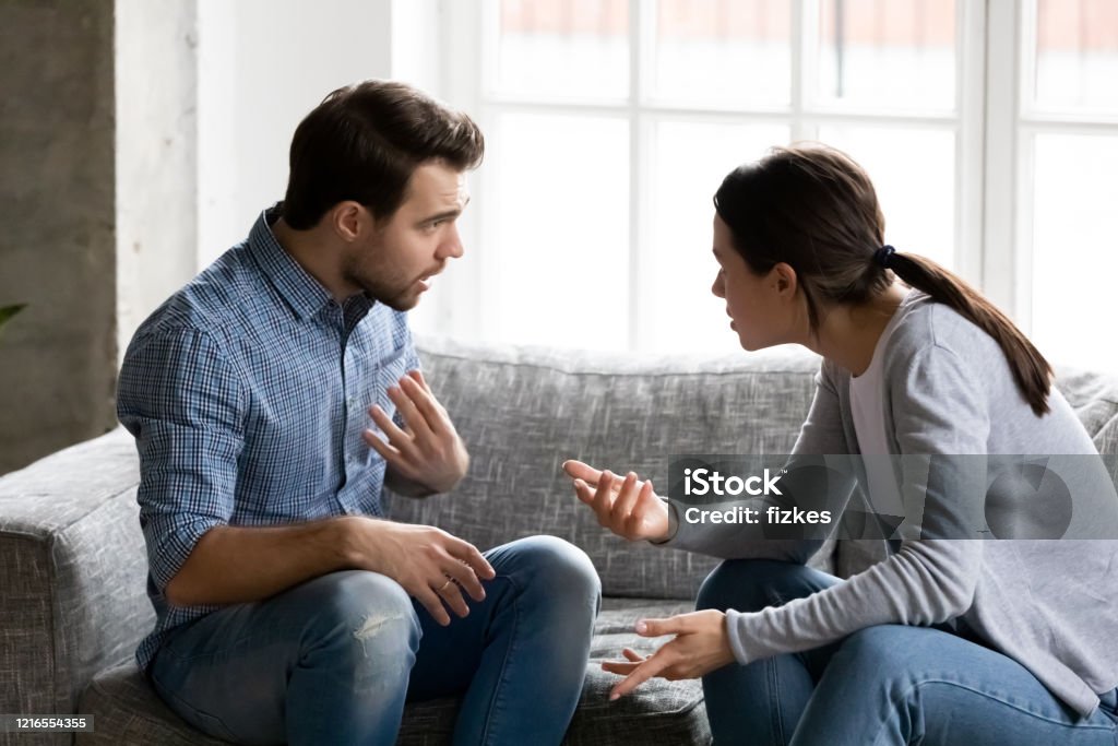 Stressed young married family couple arguing, blaming each other. Stressed young married family couple arguing emotionally, blaming lecturing each other, sitting on couch. Depressed husband quarreling with wife, having serious relations communication problems. Two Parents Stock Photo
