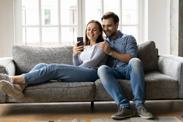 istock Happy young couple relaxing on sofa, looking at cellphone screen. 1216554425