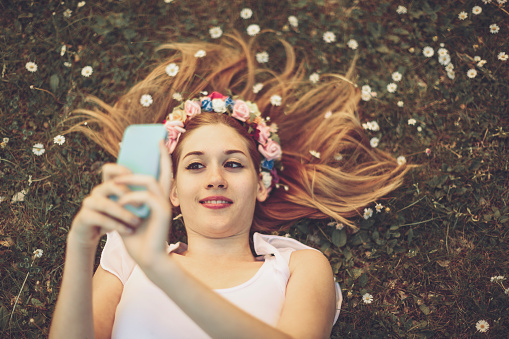 Young girl is lying in the grass and taking selfies