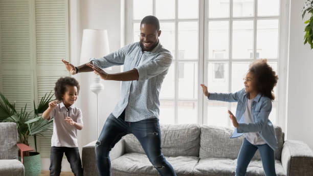 Young african ethnicity father teaches little kids to dance Happy African ethnicity father have fun teaches little preschool kids to dance in modern living room at home. Dad with son and daughter engaged in funny activity enjoy leisure carefree weekend concept dancing dad stock pictures, royalty-free photos & images