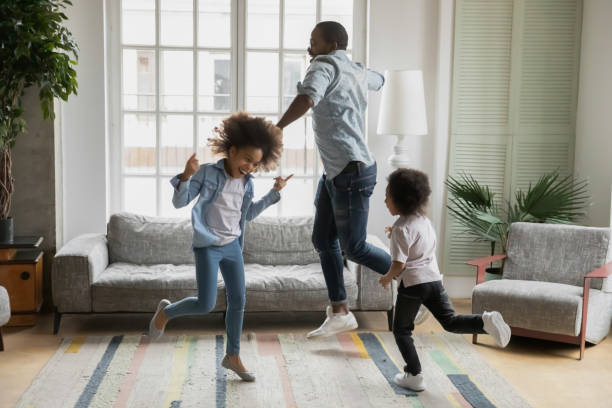 African father son and daughter listening music dancing at home Active african funny dad little son and crazy daughter heavy metal or rock and roll lovers dancing in cozy living room relish life fooling around listening cool music scream with joy enjoy party hard dancing dad stock pictures, royalty-free photos & images