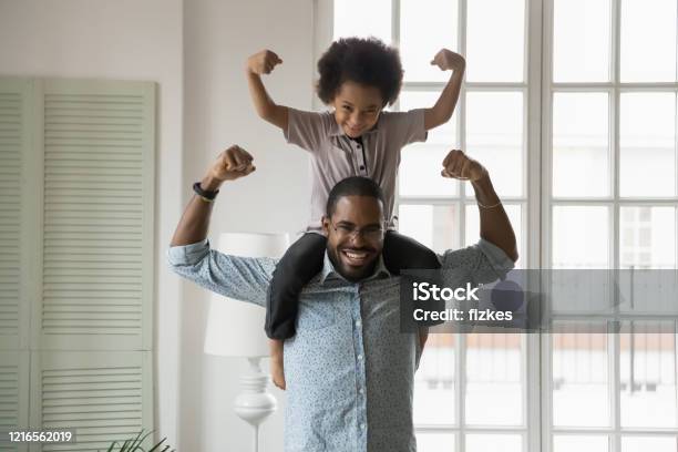 African Ethnicity Little Son Sitting On Fathers Shoulders Showing Biceps Stock Photo - Download Image Now