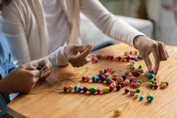 Closeup mom and daughter making handmade bangles with wooden beads Close up african mom and daughter making handmade bangles, charms using cord and wooden natural material diverse color beads improve fine motor skills and promote coordination pastime activity concept Bead stock pictures, royalty-free photos & images