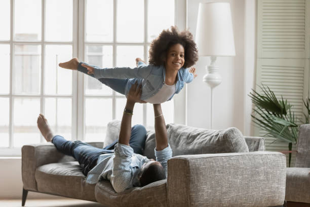 istock African father raised up daughter playing together at home 1216562049