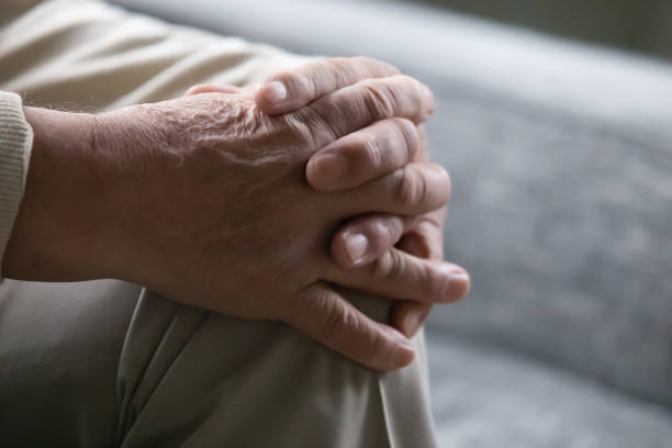 istock Old man sitting on couch palms folded on knee closeup 1216570452