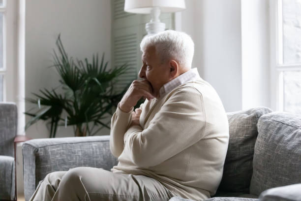 istock Lonely old man sitting on couch lost in pessimistic thoughts 1216570454