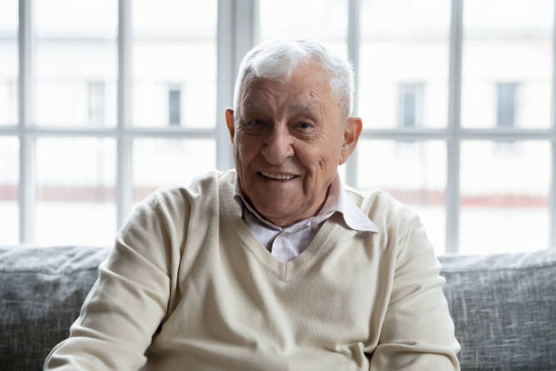 istock Old healthy positive grandfather sitting on couch looking at camera 1216570459