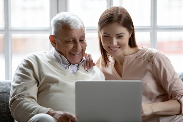 istock Grownup daughter and 80s father sit on couch with laptop 1216570532