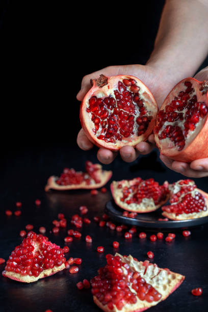 Two halves of pomegranate in male hands. On the table is a pomegranate.