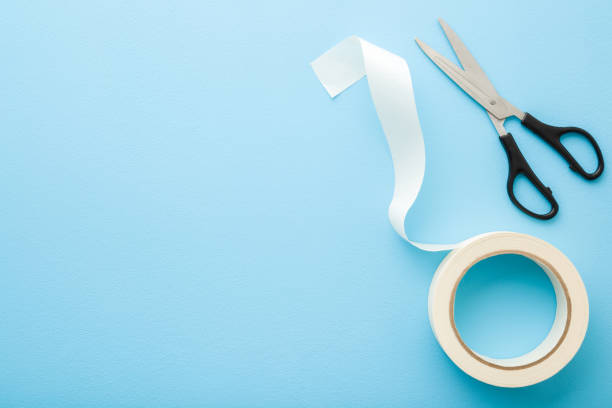 istock White roll of scotch and scissors on light blue table background. Pastel color. Closeup. Empty place for text. Top down view. 1216573939