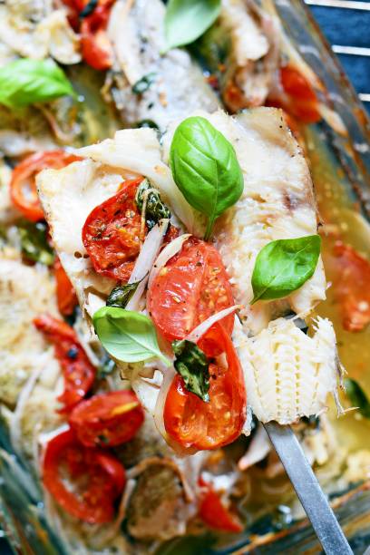 White fish (pollock, cod, hake) baked with tomatoes, Italian herbs and fresh basil leaves in basil in their own juice. Delicious Mediterranean seafood dinner. White fish (pollock, cod, hake) baked with tomatoes, Italian herbs and fresh basil leaves in basil in their own juice. Delicious Mediterranean seafood dinner. merluza stock pictures, royalty-free photos & images